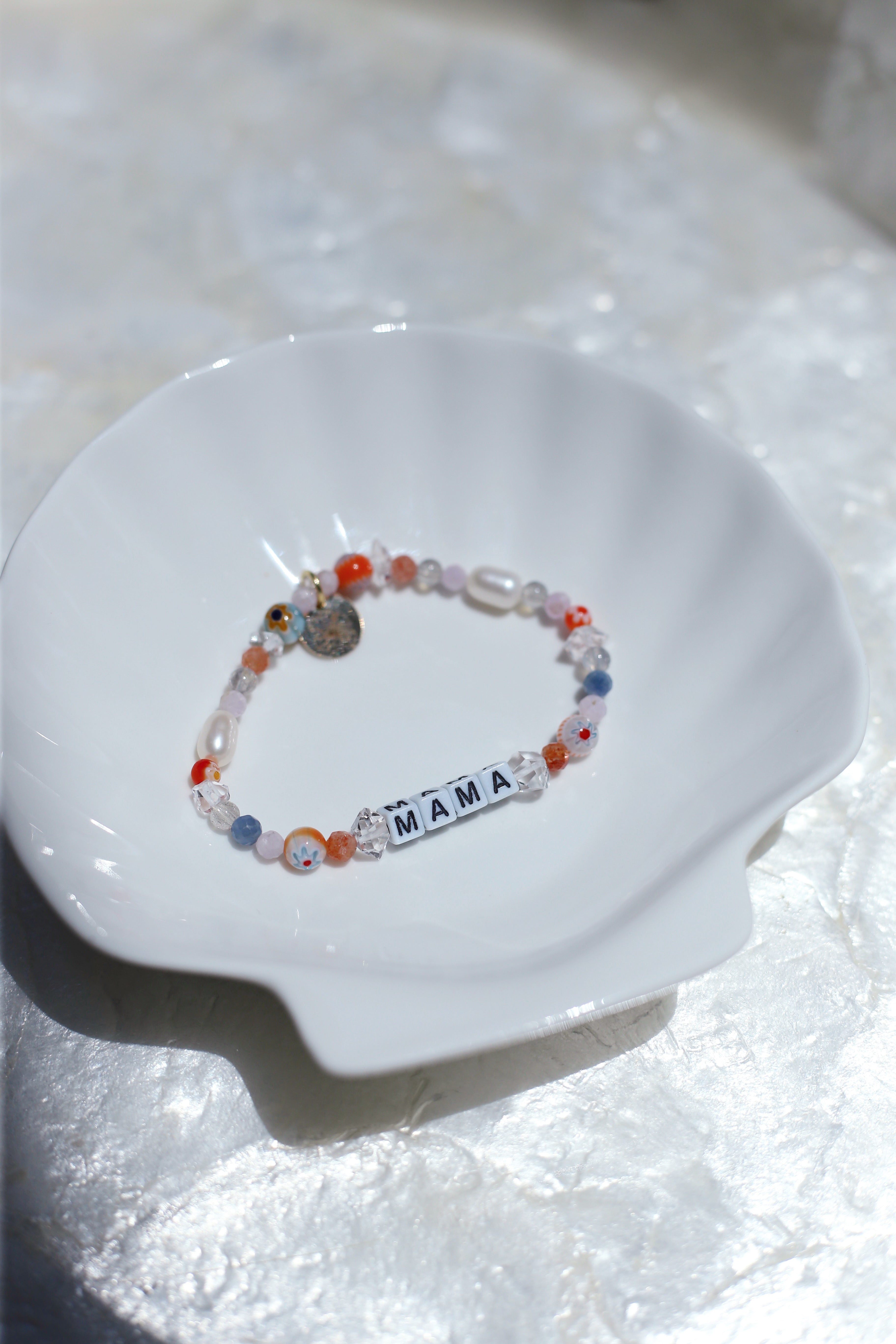 Tangerine customizable gemstone bracelet (spelling 'MAMA') on a white dish