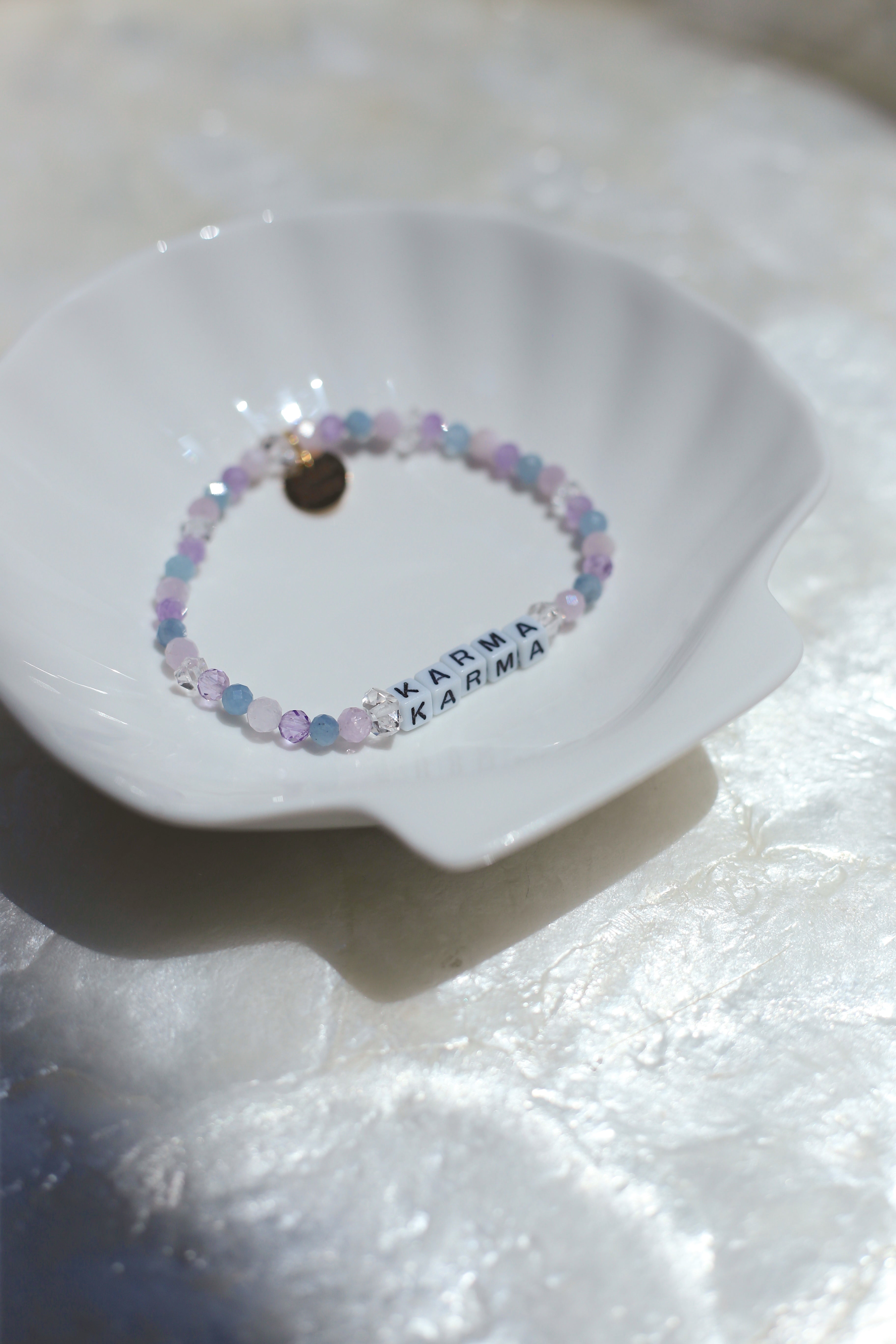 Cotton Candy customizable pastel gemstone bracelet with letters spelling 'KARMA' on a white dish