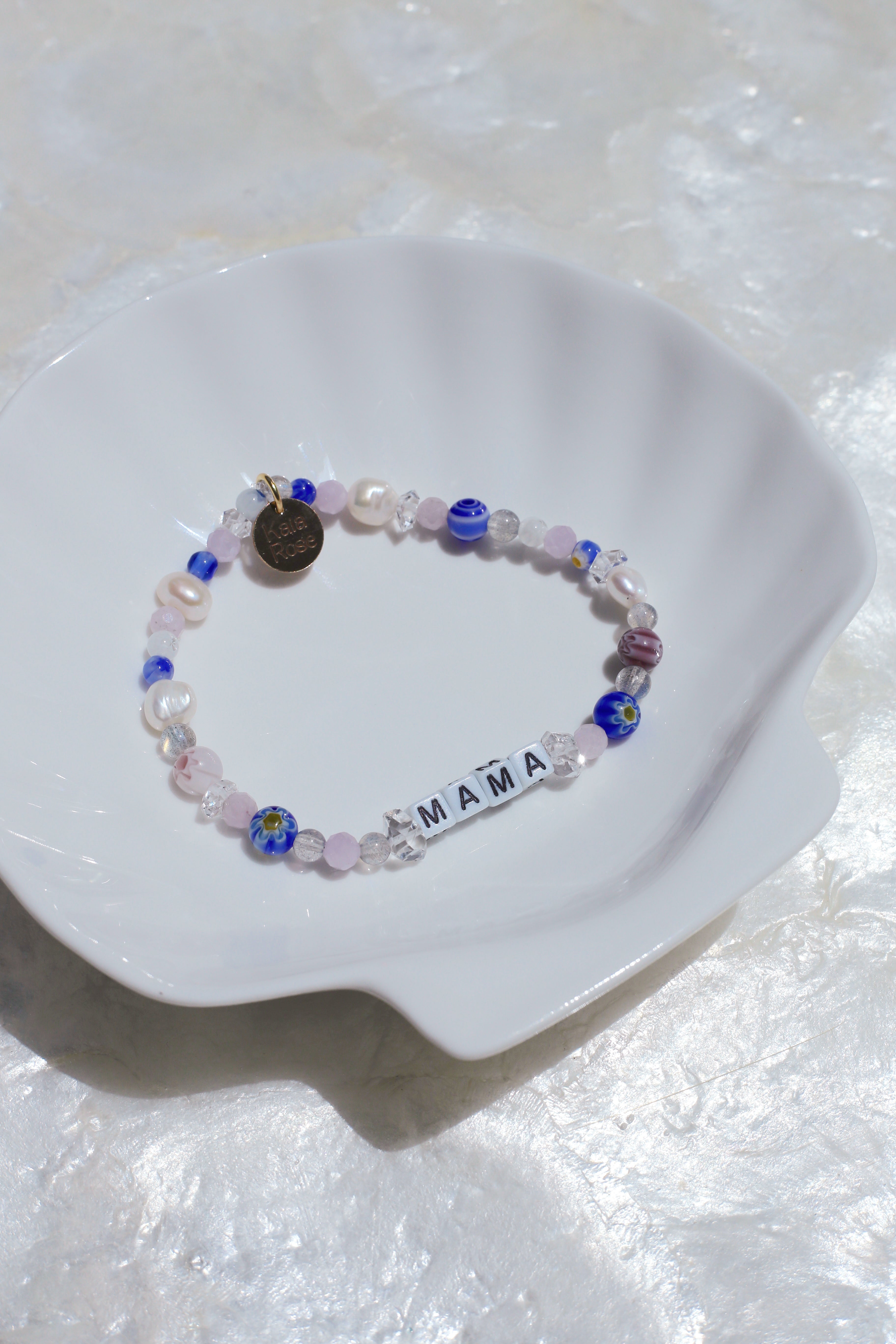 Florence customizable gemstone word bracelet (spelling 'MAMA') on a white shell dish