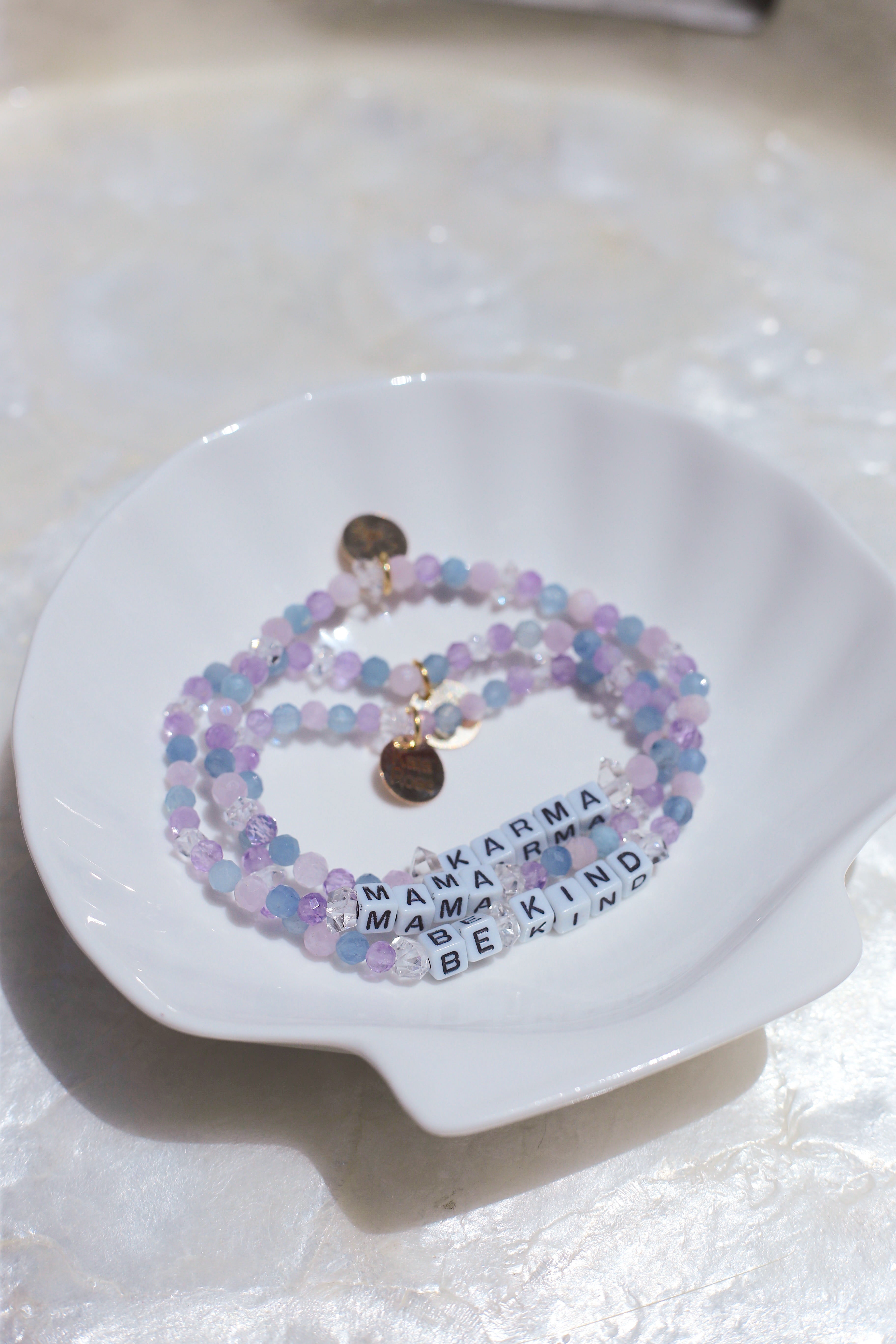 Stack of Cotton Candy pastel gemstone bracelets with letter charms on a white dish